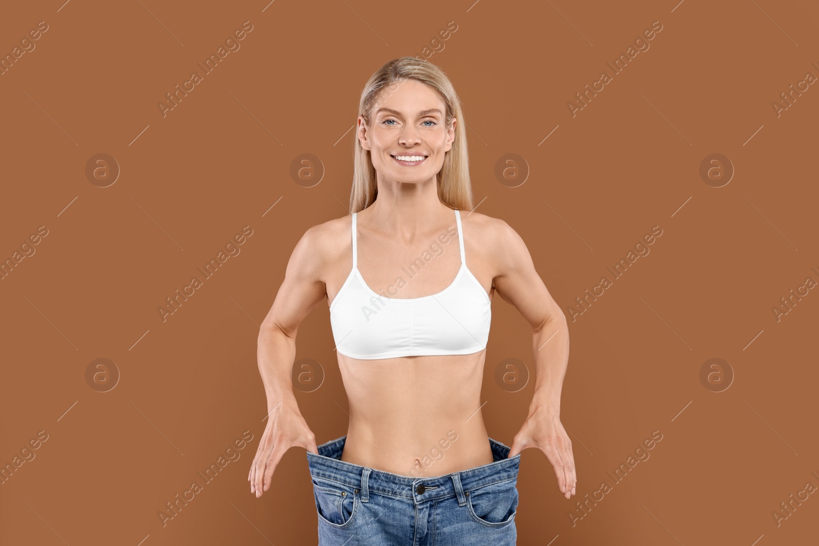 Photo of Slim woman wearing big jeans on brown background. Weight loss