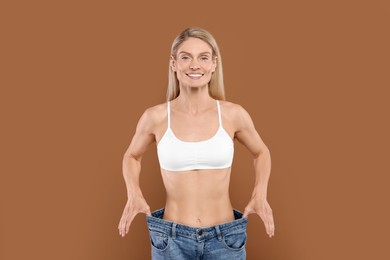 Photo of Slim woman wearing big jeans on brown background. Weight loss