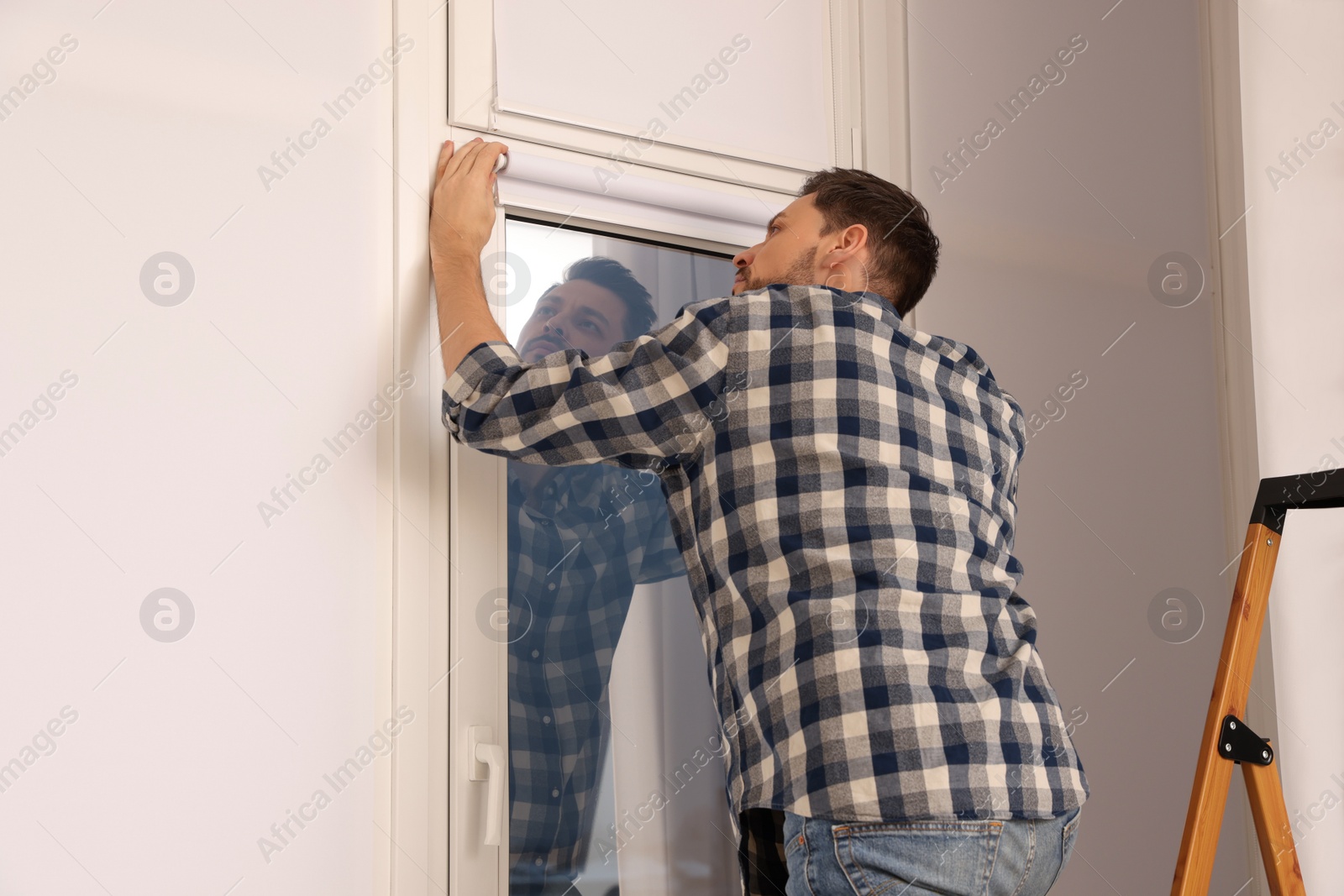 Photo of Man installing modern roller window blind indoors