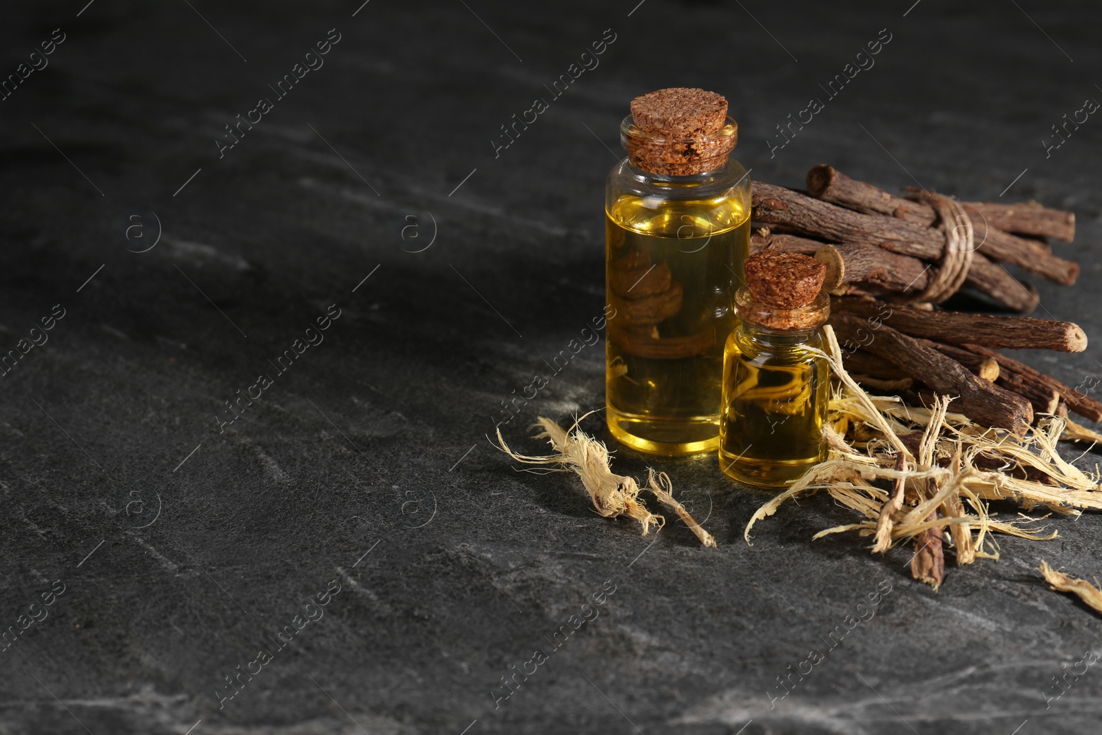 Photo of Dried sticks of licorice root and bottles with essential oil on black textured table. Space for text