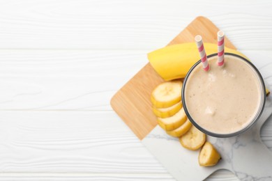 Glass of tasty banana smoothie with straws and fresh fruit on white wooden table, top view. Space for text