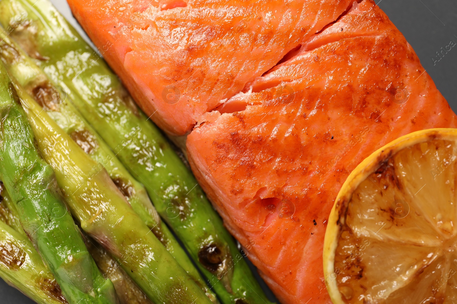 Photo of Tasty grilled salmon with asparagus and lemon on grey plate, top view