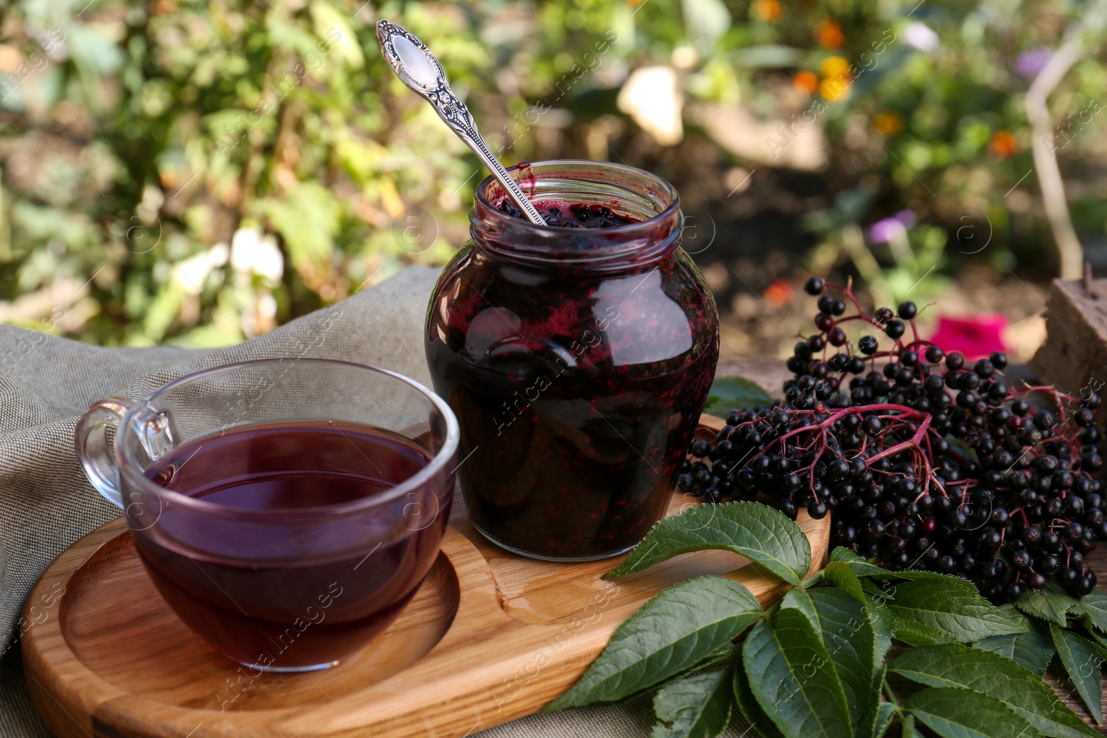 Photo of Elderberry jam, glass cup of tea and Sambucus berries on table outdoors