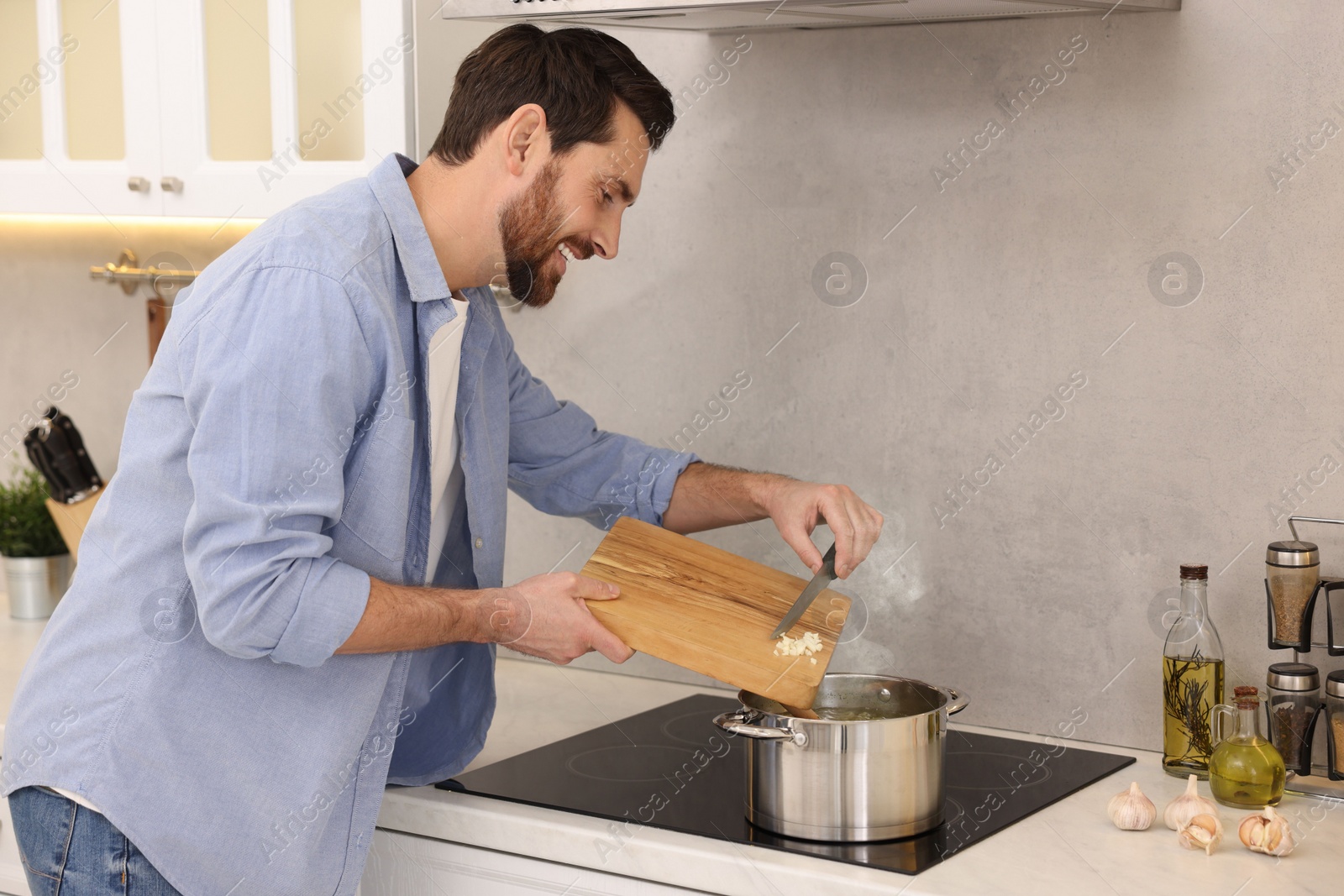 Photo of Man adding garlic into soup in kitchen