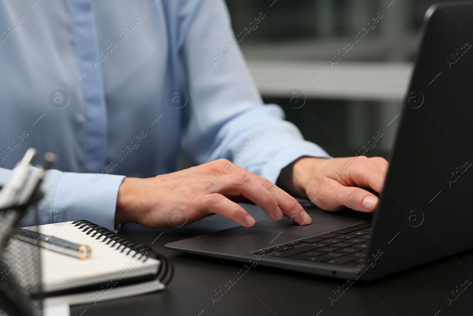 Photo of Woman working on laptop at black desk in office, closeup