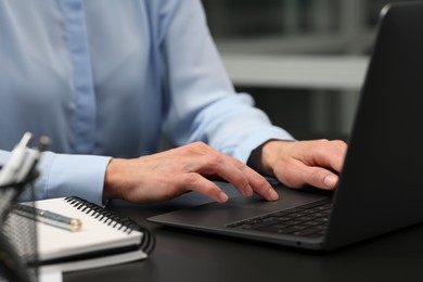 Woman working on laptop at black desk in office, closeup