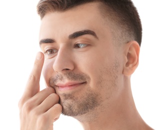 Photo of Young man putting contact lens in his eye on light background