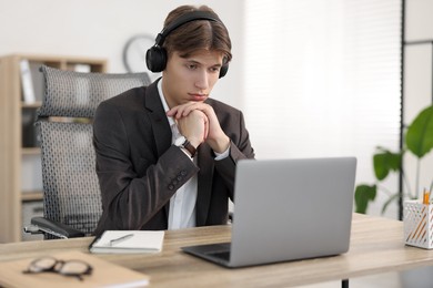 Man in headphones watching webinar at wooden table in office