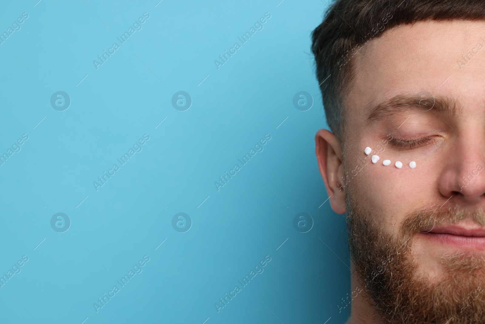 Photo of Handsome man with moisturizing cream on his face against light blue background, closeup. Space for text