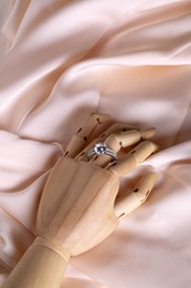 Photo of Elegant jewelry. Wooden mannequin hand with luxury ring on pink cloth, top view