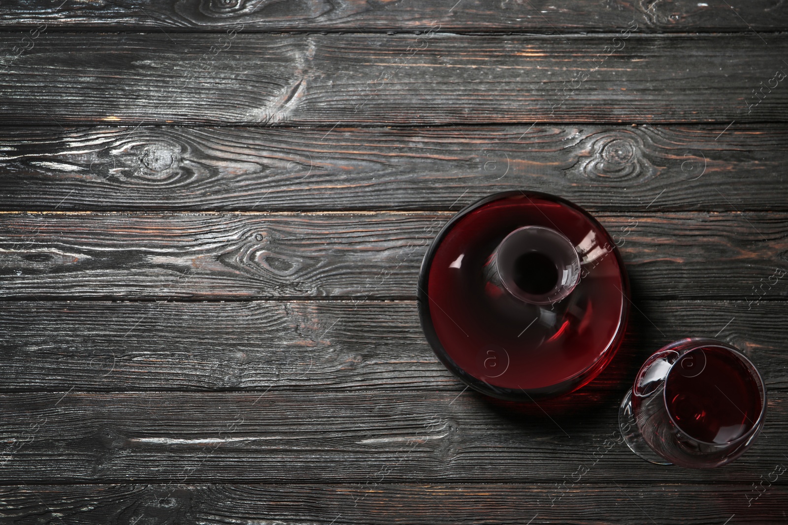 Photo of Decanter and glass with red wine on wooden background, top view
