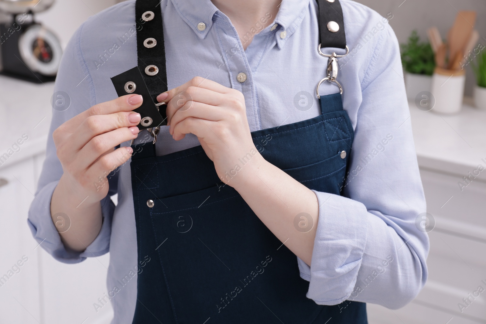 Photo of Woman putting on apron in kitchen , closeup