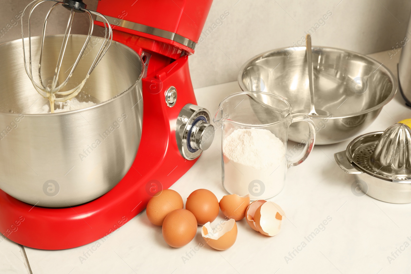 Photo of Modern red stand mixer, different ingredients and squeezer on white marble table