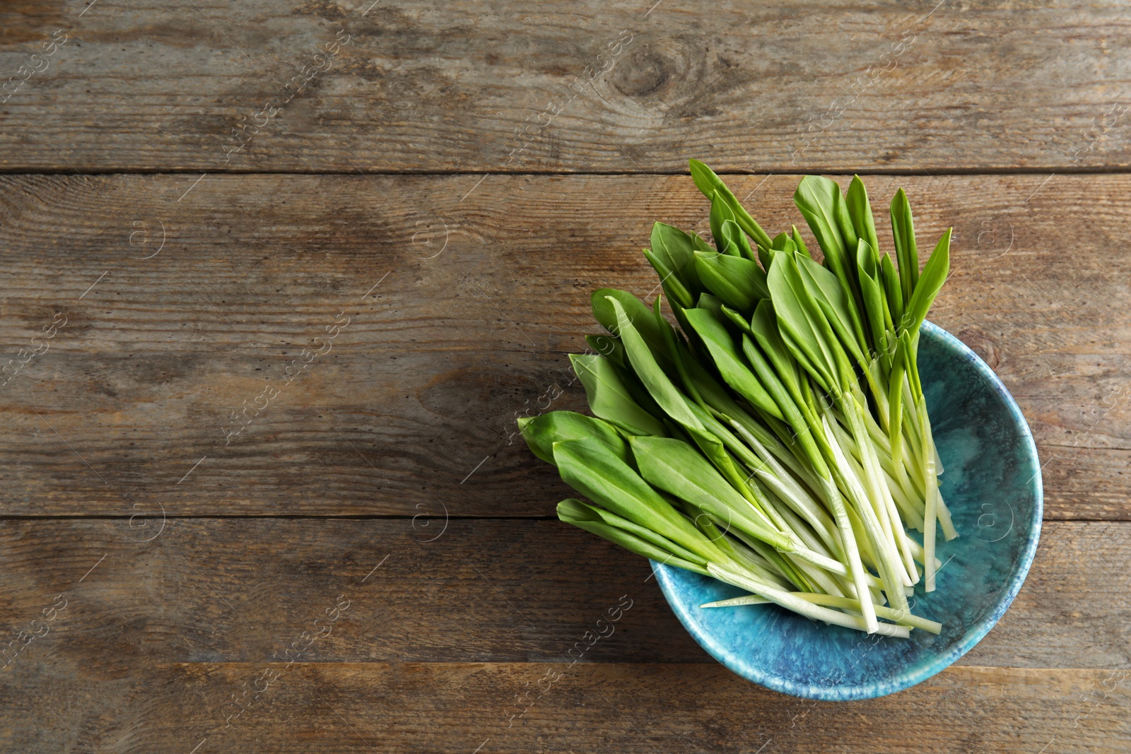 Photo of Bowl with wild garlic or ramson on wooden table, top view. Space for text