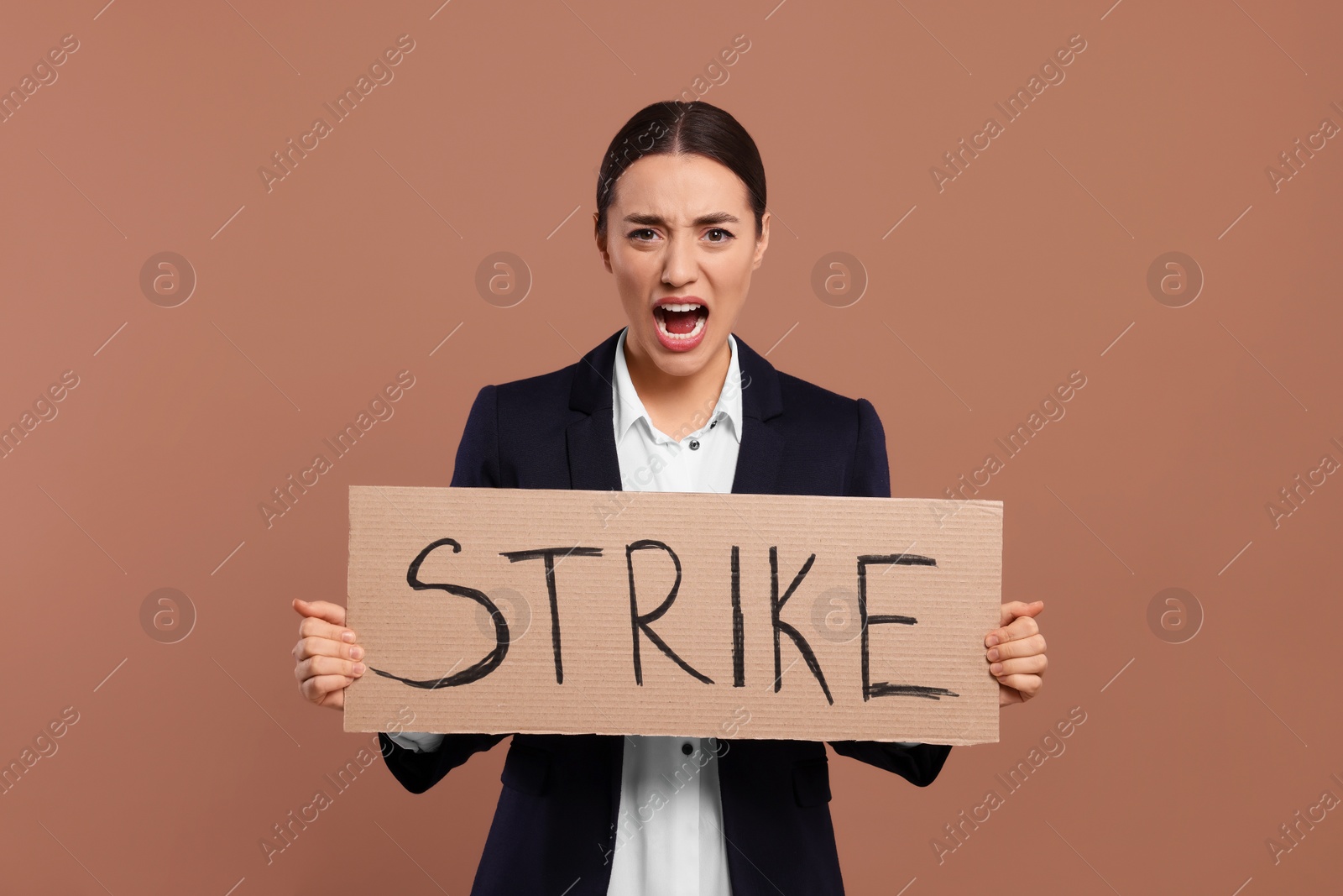 Photo of Angry young woman holding cardboard banner with word Strike on brown background