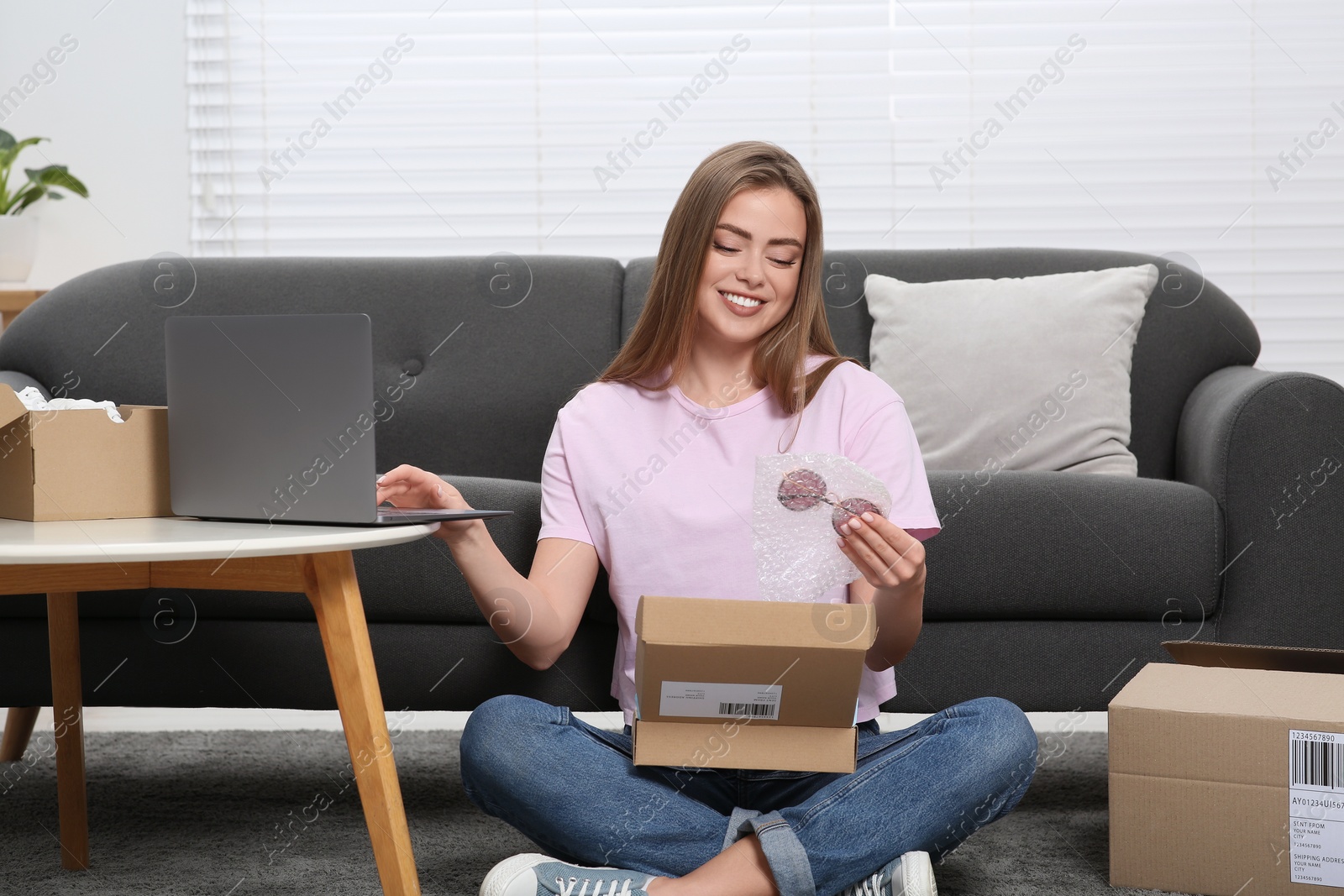 Photo of Happy woman using laptop while unpacking parcel at home. Online store