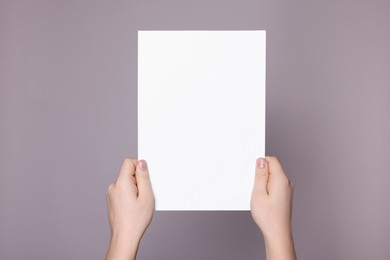 Photo of Woman holding sheet of paper on grey background, closeup. Mockup for design