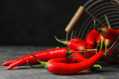 Photo of Red hot chili peppers and metal basket on grey table, closeup. Space for text
