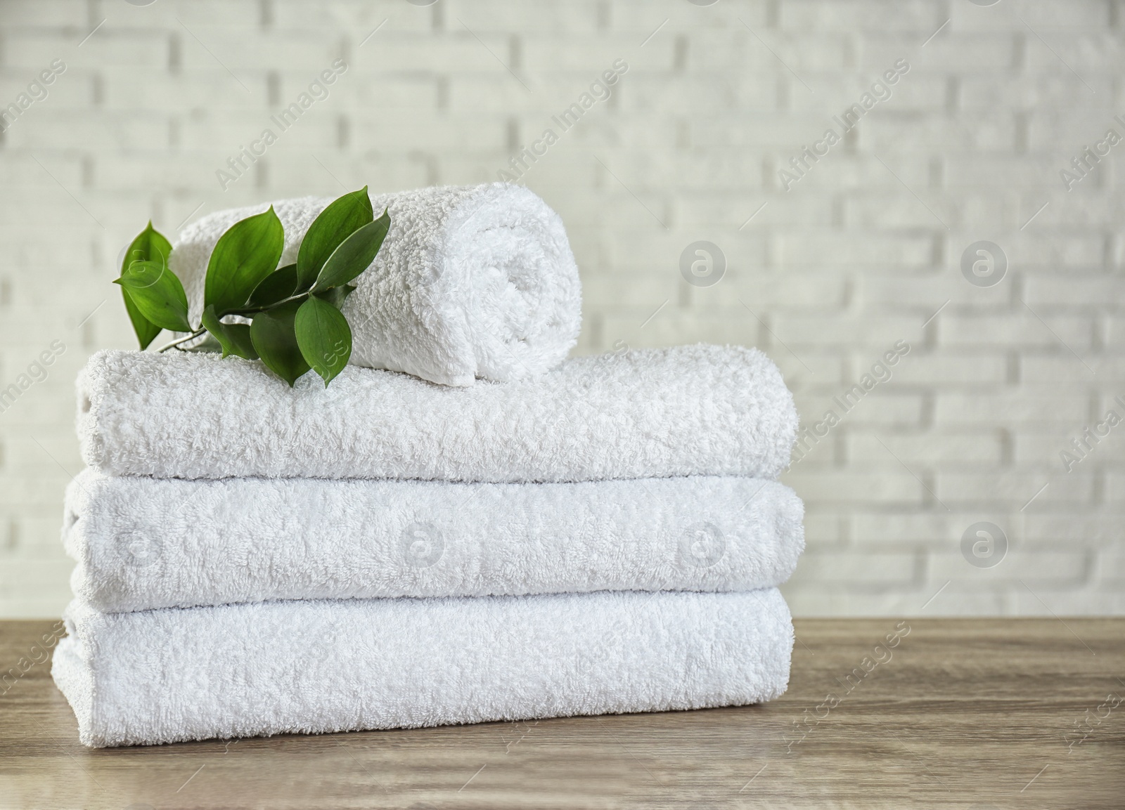 Photo of Clean bath towels and green branch on wooden table  near white brick wall