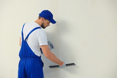 Professional worker plastering wall with putty knives indoors. Space for text