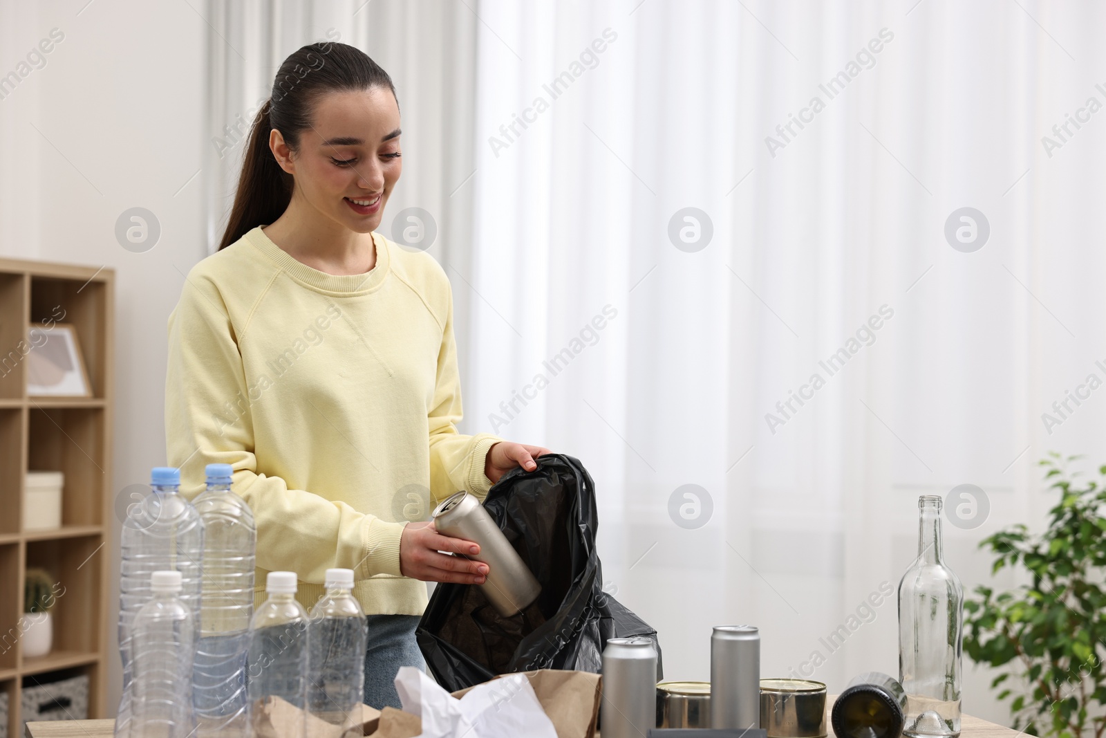 Photo of Smiling woman with plastic bag separating garbage in room. Space for text