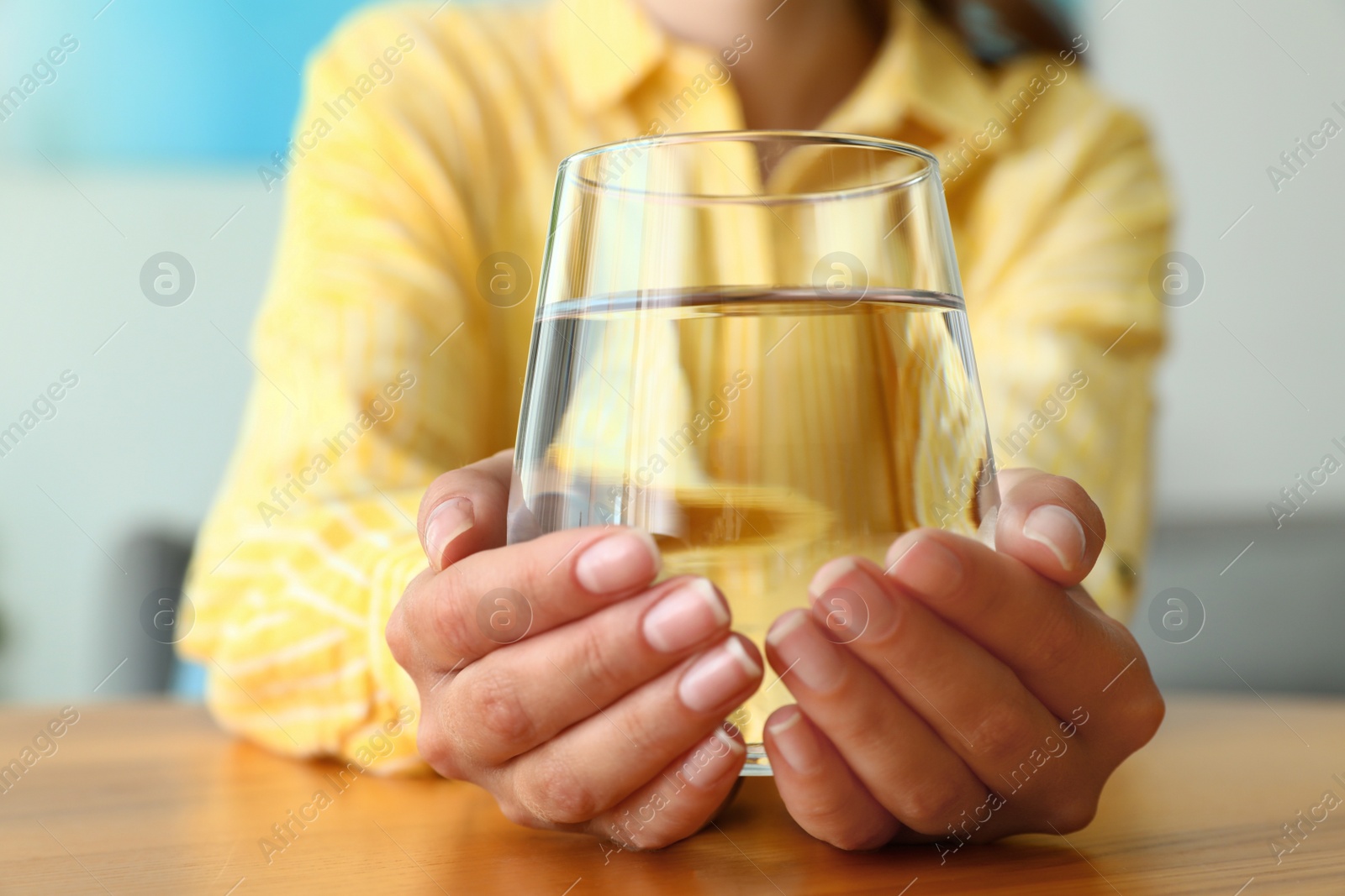 Photo of Woman holding glass of water at wooden table, closeup. Refreshing drink