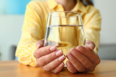 Woman holding glass of water at wooden table, closeup. Refreshing drink