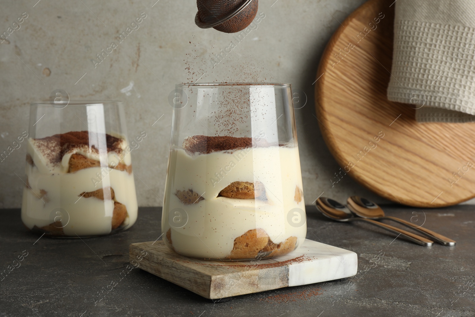 Photo of Delicious tiramisu in glasses on grey table