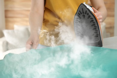 Image of Woman ironing clean laundry with steam, closeup