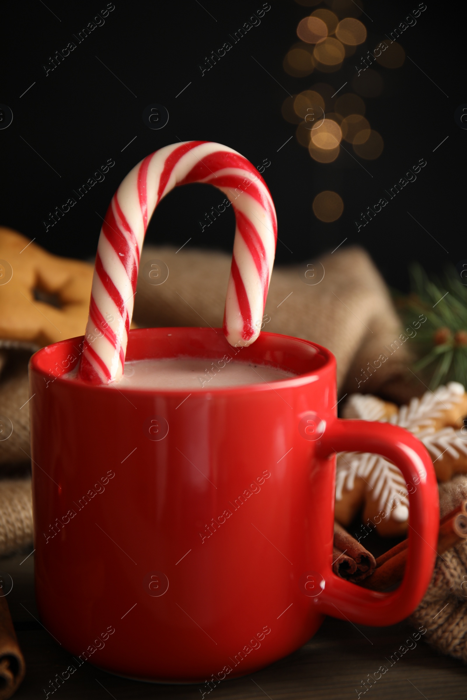 Photo of Cup of tasty cocoa with Christmas candy cane on wooden table against blurred festive lights