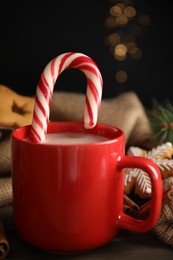 Photo of Cup of tasty cocoa with Christmas candy cane on wooden table against blurred festive lights