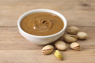 Delicious nut butter in bowl and pistachios on wooden table