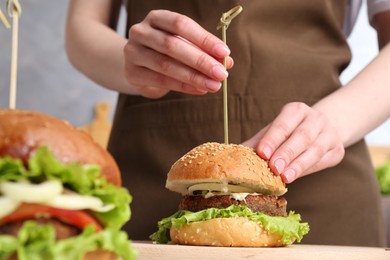 Photo of Woman making delicious vegetarian burger at table, closeup