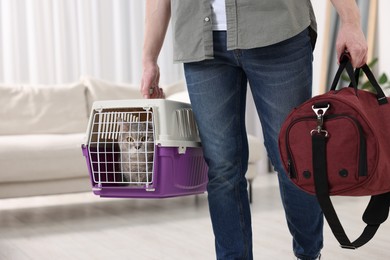 Photo of Travel with pet. Man holding carrier with cute cat and bag at home, closeup