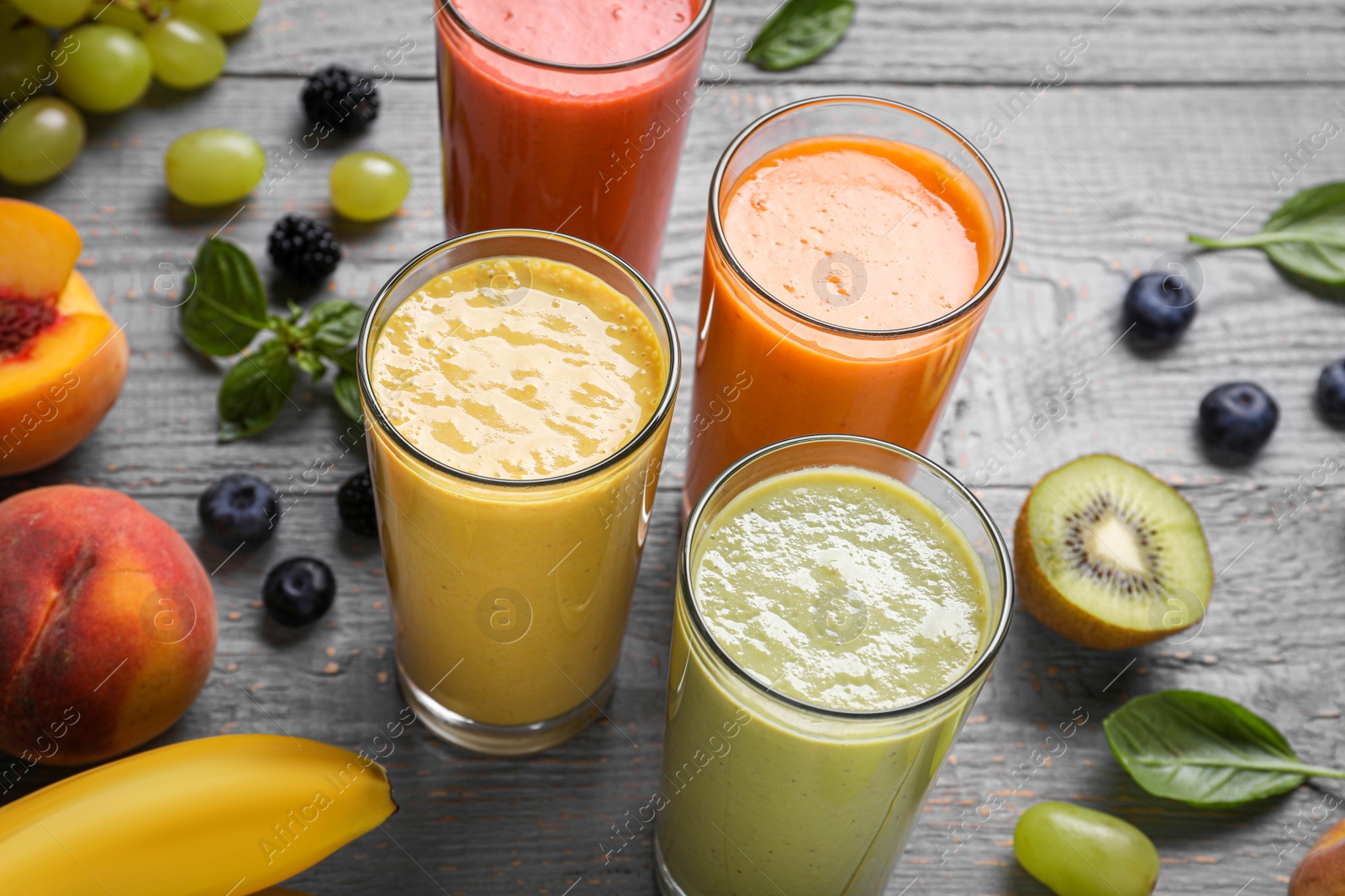 Photo of Many different delicious smoothies and ingredients on grey wooden table