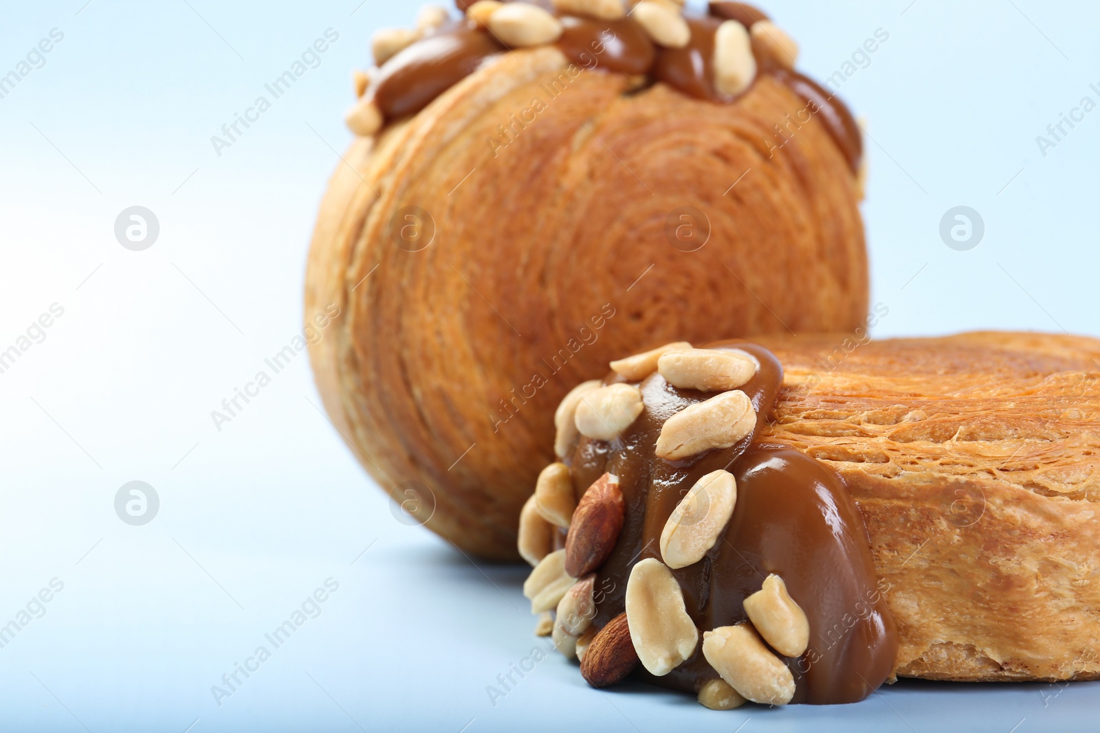 Photo of Tasty puff pastry. Supreme croissants with chocolate paste and nuts on light blue background, closeup. Space for text