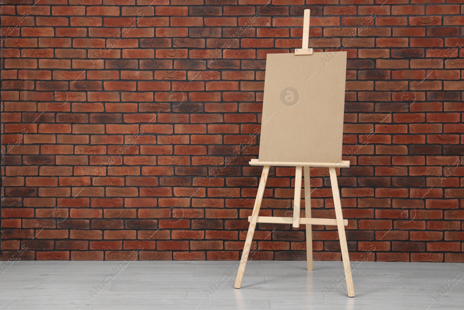 Photo of Wooden easel with blank board near brick wall indoors. Space for text