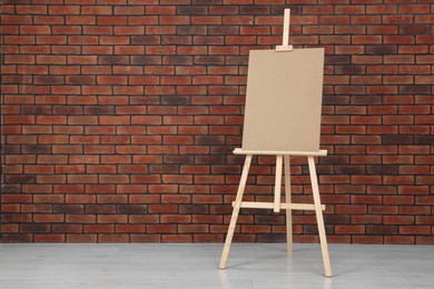 Wooden easel with blank board near brick wall indoors. Space for text