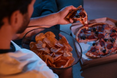 Photo of Man eating chips and pizza while watching TV on sofa at night, closeup. Bad habit