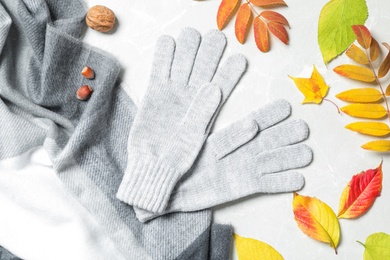 Stylish woolen gloves, scarf and dry leaves on white table, flat lay