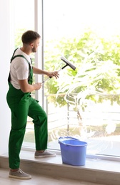 Male cleaner wiping window glass with squeegee indoors