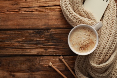 Photo of Flat lay composition with cup of coffee and knitted scarf on wooden table, space for text. Cozy winter