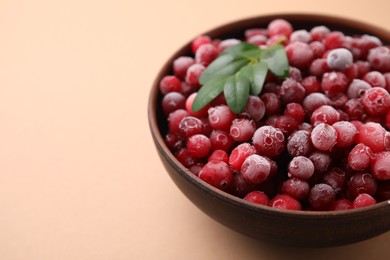 Photo of Frozen red cranberries and green leaves on beige background, closeup. Space for text