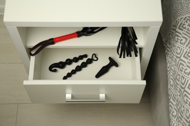 Photo of Bedside table with black leather whip, anal plug and beads indoors. Sex toys