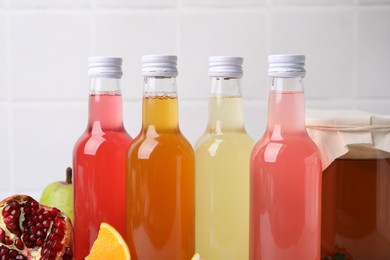 Photo of Delicious kombucha in glass bottles, jar and fresh fruits against white tiled background