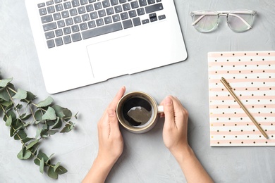 Photo of Young woman with cup of delicious coffee at table, top view