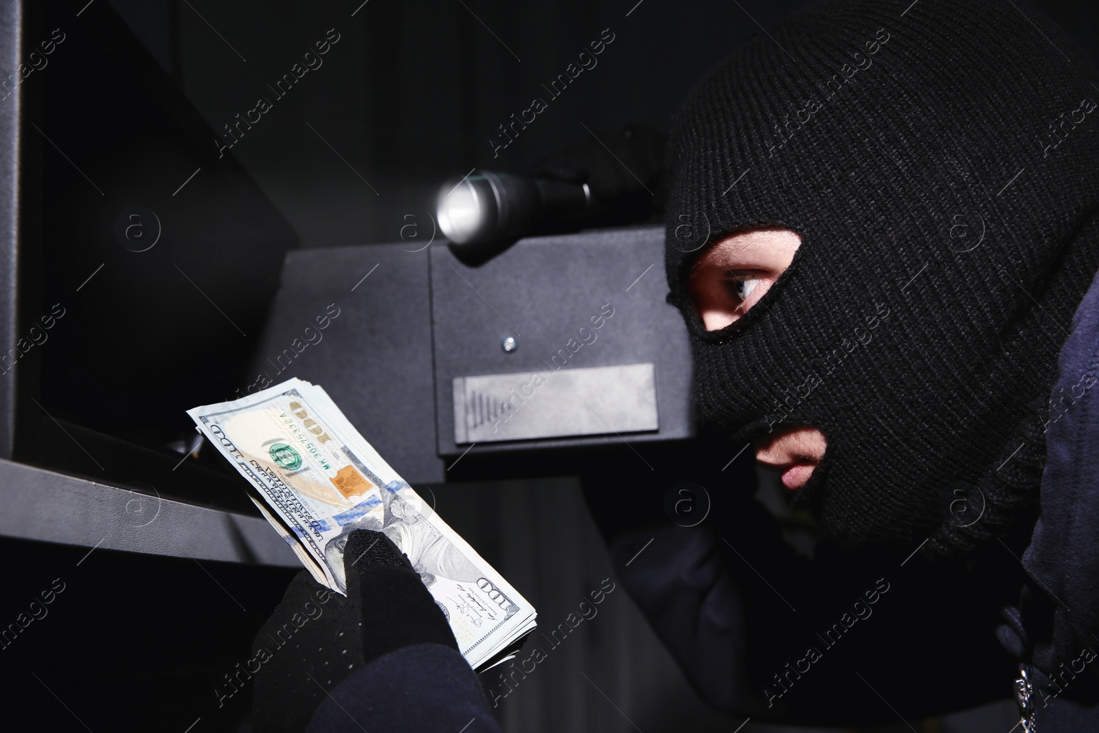 Photo of Thief taking money out of steel safe indoors at night, closeup