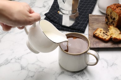 Woman pouring milk into cup of coffee at white marble table, closeup