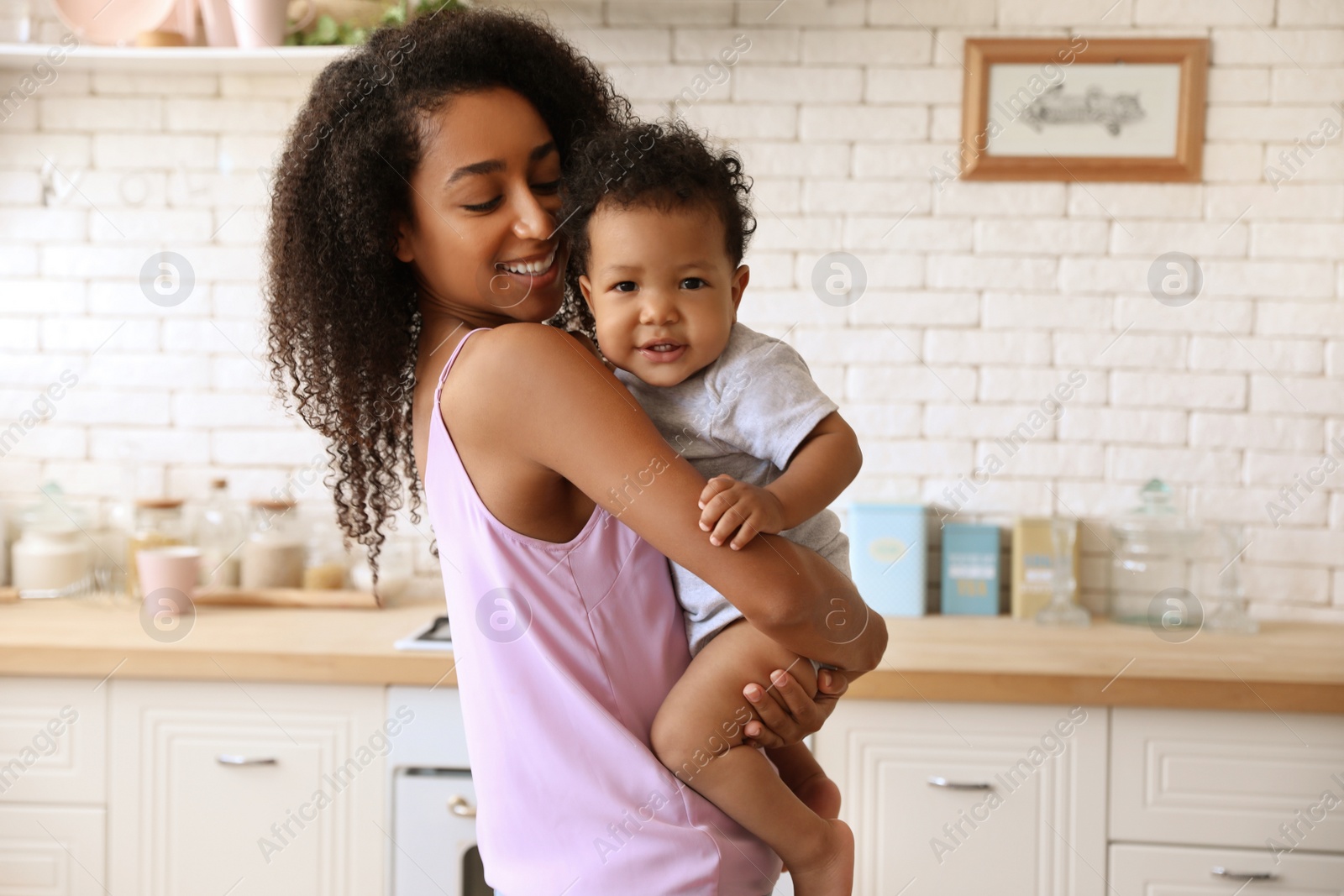 Photo of African-American woman with her baby in kitchen. Happiness of motherhood