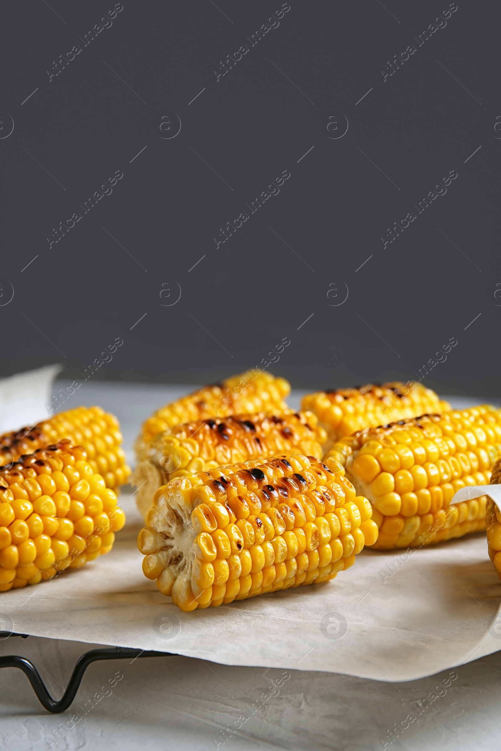 Photo of Cooling rack with grilled corn cobs on table against gray background. Space for text